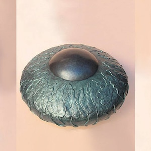 May include: A teal ceramic lidded box with a textured leaf design. The lid has a dark blue center.