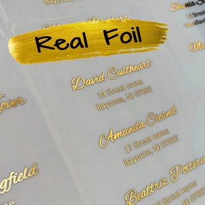 May include: Gold foil address labels with names and addresses printed on them. The labels are on a clear background. The text on the labels is "Real Foil".
