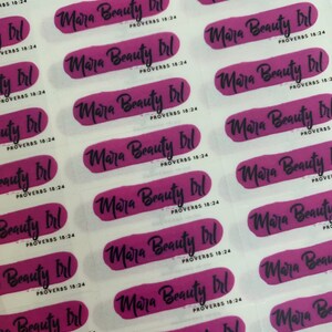 May include: A sheet of stickers with the text "Mara Beauty Irl" and "Proverbs 18:24" repeated on each sticker. The stickers are pink and white with a brushstroke effect.