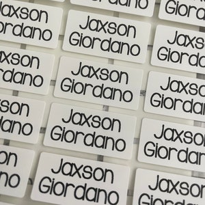 以下が含まれることがあります： 「Jaxson Giordano」と黒で印刷された、白い長方形のラベルが複数あるクローズアップ。