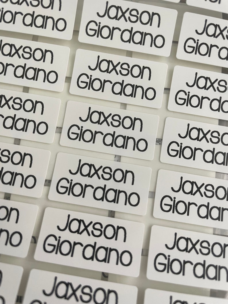 以下が含まれることがあります： 「Jaxson Giordano」と黒で印刷された、白い長方形のラベルが複数あるクローズアップ。