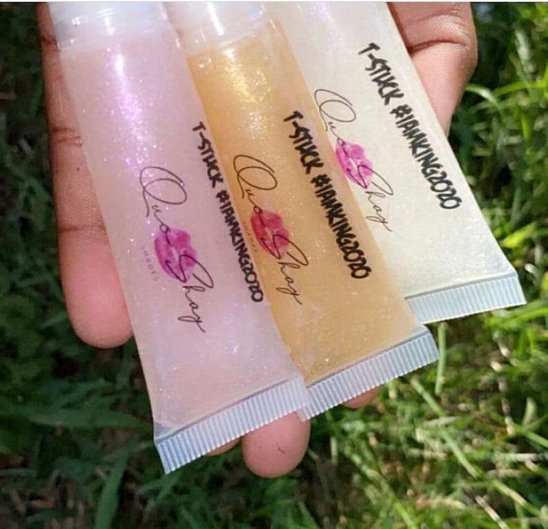 May include: Three clear lip gloss tubes with a glittery texture. Each tube has a white label with the text "T-STUCK #IAMKING2020" and "Quo Shay" printed on it.