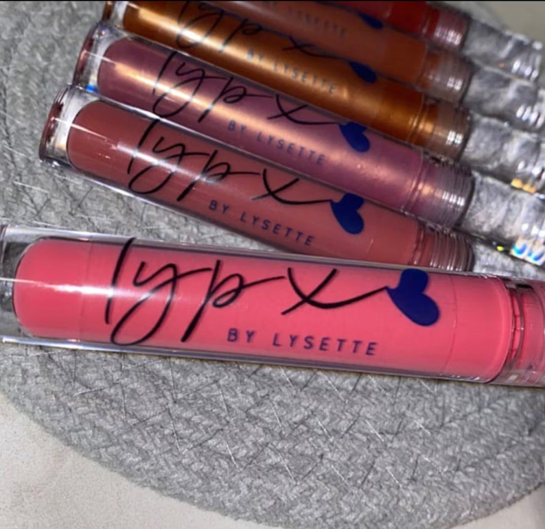 May include: A close-up of a set of lip glosses in various shades of pink and brown. The tubes are clear with a black and white logo that says "lyp x by lysette".