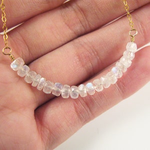 May include: A delicate gold chain necklace with a row of iridescent white moonstone beads.