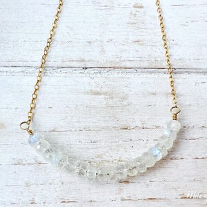 May include: A delicate gold chain necklace with a crescent-shaped row of white moonstone beads.