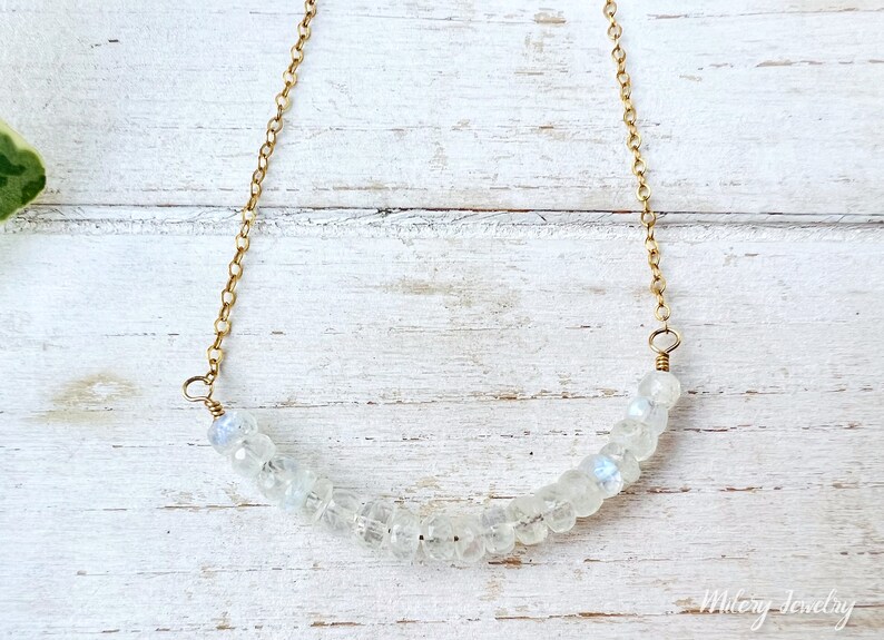 May include: A delicate gold chain necklace with a crescent-shaped row of white moonstone beads.