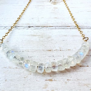 May include: A gold chain necklace with a row of iridescent white moonstone beads.