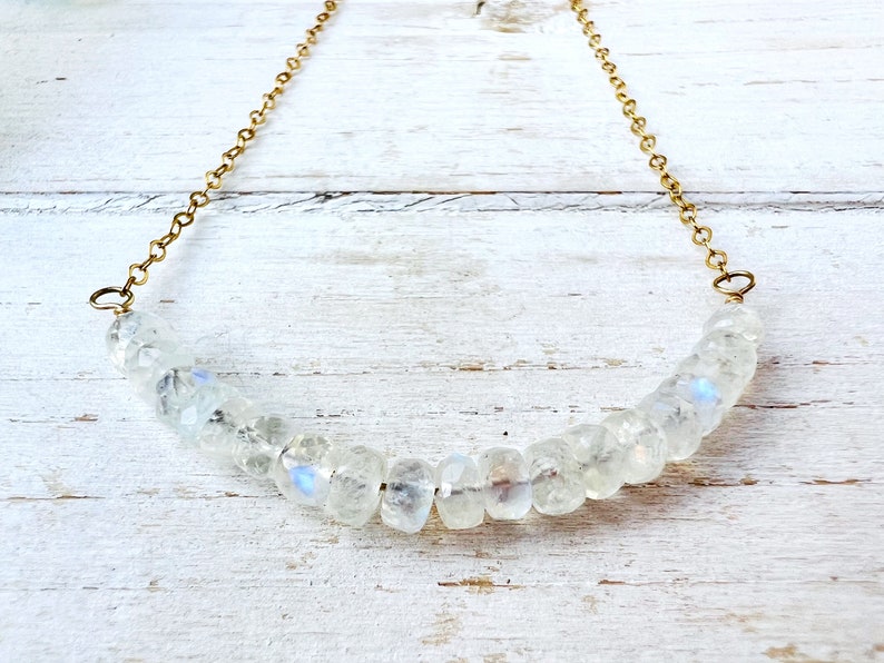 May include: A gold chain necklace with a row of iridescent white moonstone beads.
