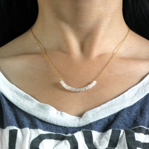 May include: A gold chain necklace with a curved row of white beads.