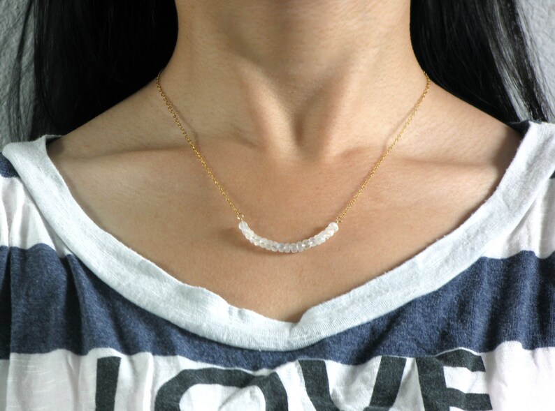 May include: A gold chain necklace with a curved row of white beads.