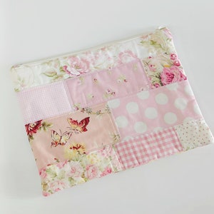 Puede incluir: Una bolsa de cremallera rosa de patchwork con un diseño floral y de mariposas.