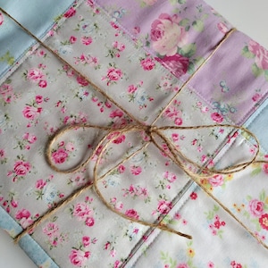 以下が含まれることがあります： ピンク、ブルー、ホワイトの花柄の入ったパッチワークキルト。キルトは紐で結ばれており、素朴でヴィンテージな雰囲気です。