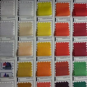Peut inclure: Un nuancier de tissus pr&eacute;sentant des &eacute;chantillons de diff&eacute;rentes couleurs, notamment blanc, jaune, orange et rouge. Le nuancier comprend des &eacute;tiquettes de texte telles que "FH2WTA White" et "FH2FYE FM Yellow". Le logo Bainbridge International est visible.