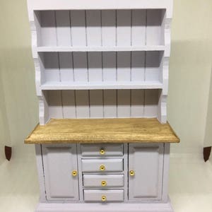 May include: A light purple wooden hutch with a top shelf and two doors with gold knobs. The hutch has four drawers with gold knobs and a wooden top.