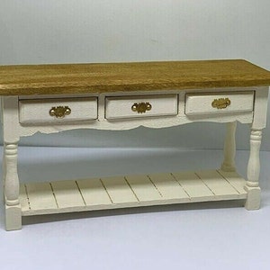 Op de afbeelding: Een wit geschilderde houten consoletafel met drie laden en een onderplank. Het tafelblad is van natuurlijke houtkleur.