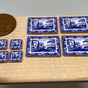 Könnte beinhalten: Miniatur-Keramikplatten und Untersetzer in Blau und Weiß mit Landschaftsmotiv. Das Set umfasst rechteckige und quadratische Teile, die an klassische Porzellanmuster erinnern. Eine Münze dient als Größenvergleich.