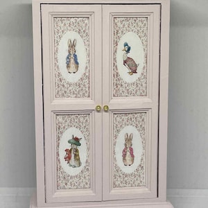 Mueble armario para casa de muñecas en miniatura a escala 1:12 pintado a mano en rosa pálido y acabado con calcomanías con temática de Beatrix Potter.