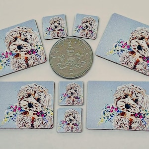 May include: A collection of square and rectangular coasters featuring a fluffy dog illustration with a floral collar. The dog is light brown and white, set against a light blue background. A coin is in the center.
