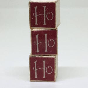 Puede incluir: Tres bloques de madera rojos apilados uno encima del otro. Cada bloque tiene la palabra "Ho" escrita en blanco en la parte delantera.