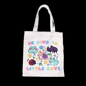 May include: White tote bag featuring colorful cartoon illustrations of a frog, snail, beetle, ladybug, and bunny. The text "BE KIND TO LITTLE GUYS" is printed in pastel colors. The bag has two white handles.