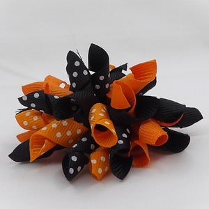 May include: A black and orange hair bow with white polka dots. The bow is made of curled ribbon and is a festive Halloween decoration.