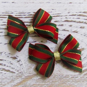 May include: Two decorative bows made of red and dark green striped ribbon with thin gold metallic threads running through the fabric. Each bow is secured in the center with a small, plain gold band. The bows are identical in design and color.