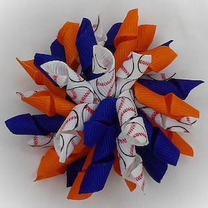 May include: A decorative hair bow featuring a baseball theme. The bow is made of orange, blue, and white ribbons. The white ribbons are printed with baseball stitching. The bow is a spiral shape.