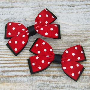 May include: Two red and white polka dot hair bows with black trim. The bows are tied together in the center with a black ribbon.