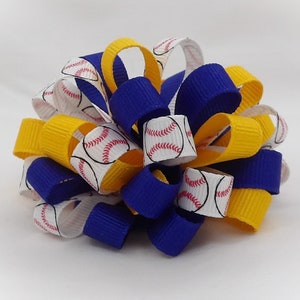 May include: A baseball-themed hair bow featuring a mix of colors. The bow is made of layered ribbons in royal blue, yellow, and white. The white ribbons are printed with baseballs. The bow is a decorative accessory.