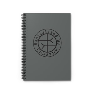 May include: A gray spiral-bound notebook with the words "Radicalized by Empathy" printed in a black circular design on the cover. The notebook is rectangular and has a black spiral binding.