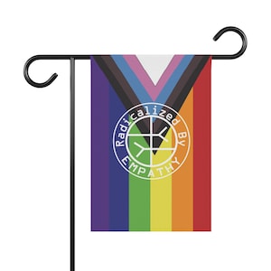 May include: A garden flag with a rainbow design and the words "Radicalized By Empathy" in a white circle. The flag has a black metal pole and hook for hanging.