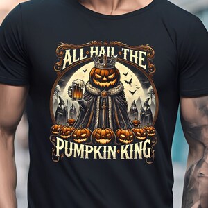 Pode incluir: Camiseta preta com um design temático de Halloween. O design apresenta um rei abóbora com coroa e cerveja, rodeado por abóboras, morcegos e o texto "ALL HAIL THE PUMPKIN KING". Um design assustador para a época.