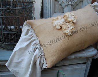May include: A burlap pillow with a white lace trim and two white lace flowers. The pillow is sitting on a light blue surface with a metal birdcage in the background. The text "www.rusticchictoyou.etsy.com" is printed on the pillow.