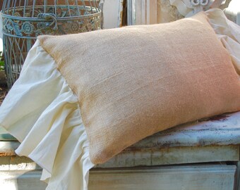 May include: A burlap pillow with a white ruffled trim. The pillow is sitting on a light blue wooden surface.