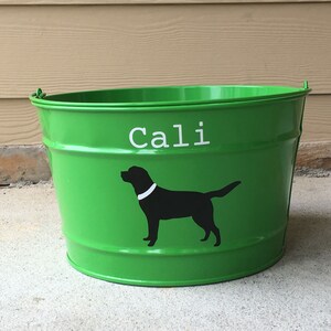 May include: Green metal bucket with the name "Cali" written in white letters and a black silhouette of a dog with a white collar.