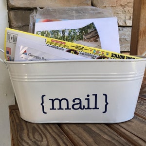May include: White metal container with handles, labeled "{mail}" in blue lettering. The container is filled with various pieces of mail, including a yellow envelope and a white envelope with the Georgia Power logo.