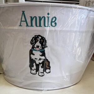 May include: White metal bucket with a black and white dog illustration and the name "Annie" printed in teal.