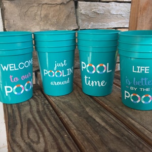 May include: Four turquoise plastic cups with different pool-themed sayings. The sayings are "Welcome to our Pool", "Just Poolin' Around", "Pool Time", and "Life is Better by the Pool".