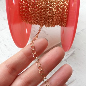 Op de afbeelding: Een spoel met een gouden ketting, gewikkeld rond een rode plastic spoel. Een hand houdt een stuk van de ketting vast, waardoor de details van de schakels zichtbaar zijn.