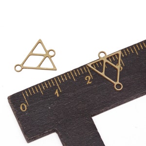 May include: Two gold-toned metal triangle charms with openwork designs and jump rings. The charms are about 1 inch in size and are shown next to a ruler.