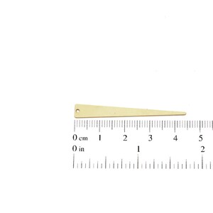May include: A gold-colored metal triangle with a hole at the top, measuring approximately 4 inches in length. The triangle is shown against a white background with a ruler for scale.