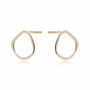 May include: A pair of gold-toned earrings with a unique, irregular oval shape. The earrings have a brushed finish and a simple post design.