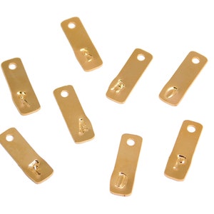 Op de afbeelding: Acht goudkleurige metalen labels met de letters A, B, D, F, H, O, P en R erop gestempeld. De labels zijn rechthoekig en hebben een gat aan de bovenkant.