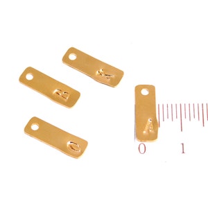 Op de afbeelding: Vier gouden metalen labels met de letters A, B en O erop gestempeld. De labels zijn ongeveer 2,5 cm lang en hebben een gat aan de bovenkant om aan een ketting of armband te bevestigen.