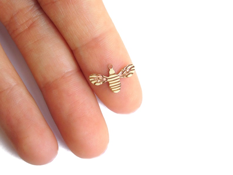 May include: A gold-colored bee charm with a striped pattern. The charm is small and delicate, perfect for adding a touch of whimsy to jewelry.