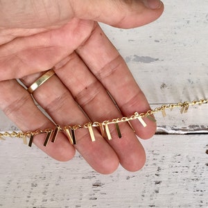 May include: Gold chain with dangling rectangular charms. The chain is held in a hand.
