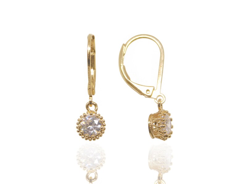 May include: A pair of gold earrings with a clear crystal stone in a gold setting. The earrings have a lever back closure.