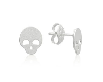 Puede incluir: Un par de pendientes de plata con forma de calavera. Los pendientes son pequeños y tienen un diseño sencillo.