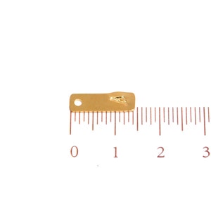 Op de afbeelding: Een gouden metalen connector met een klein gaatje in het midden. De connector is ongeveer 2,5 cm lang en wordt gemeten op een liniaal.