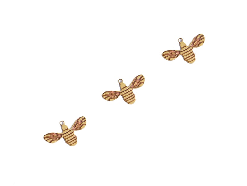 May include: Three wooden bee charms with a striped pattern in shades of brown and yellow. The bees have a small loop at the top for hanging.